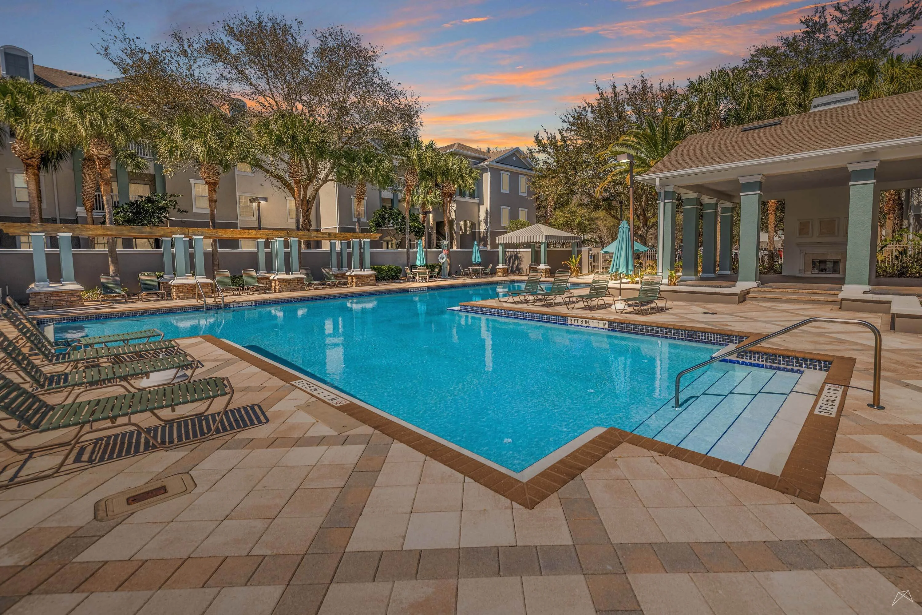 Inviting apartment pool area featuring lounge chairs, umbrellas, and a picturesque sunset backdrop.