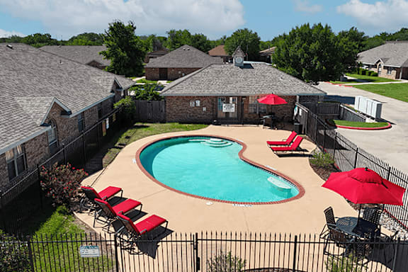 A black fence surrounds a small pool with red chairs and umbrellas.