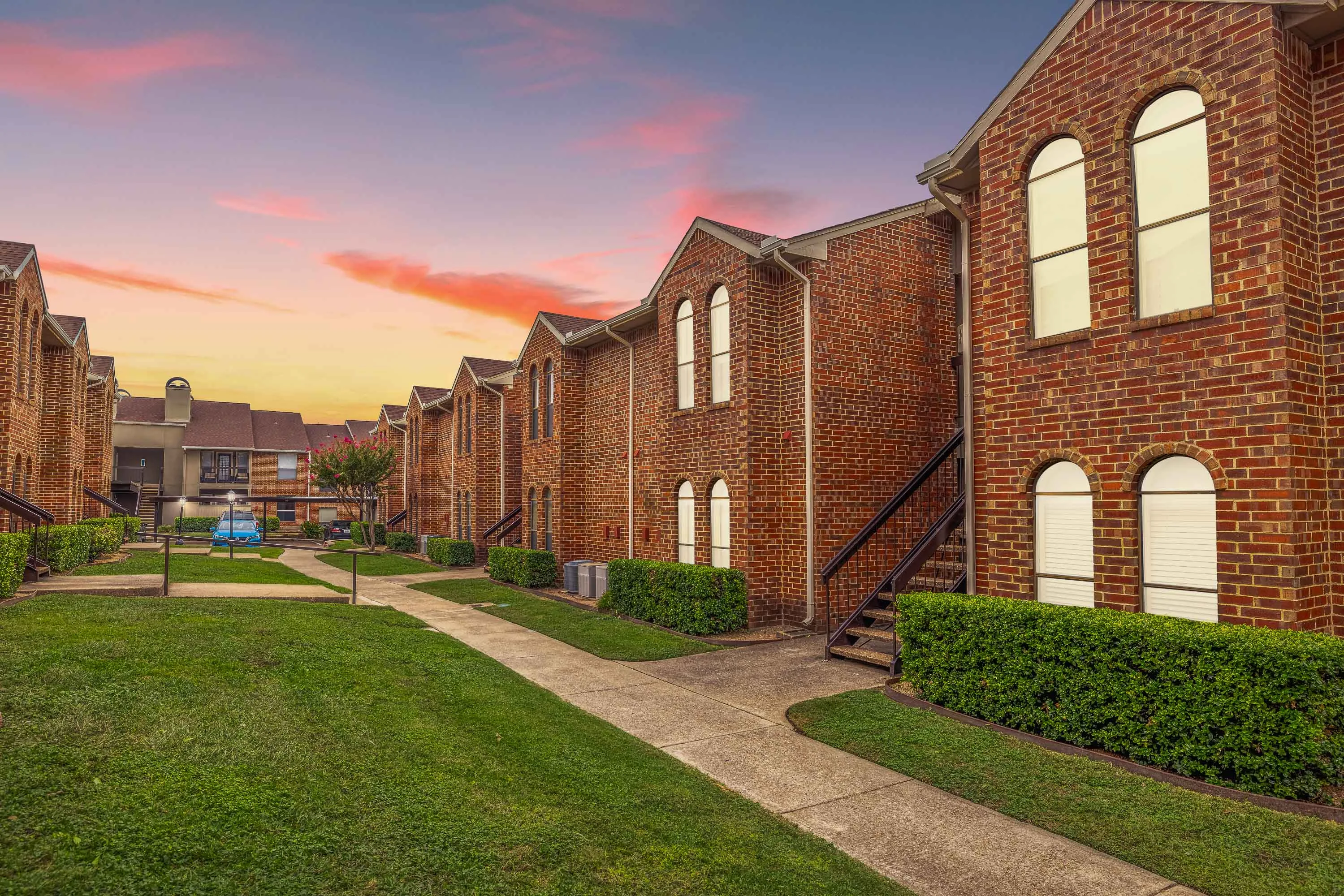 walking path between two apartment buildings with brick exterior, arched windows, and black staircases at dusk 