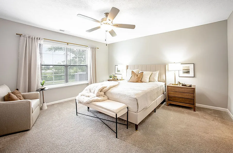 Bright and welcoming bedroom with a large window, cozy seating area, and elegant decor.