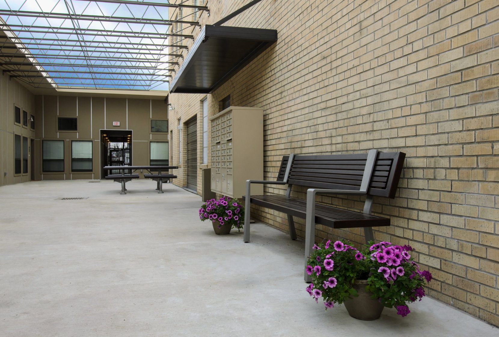 Interior courtyard with bench seating, picnic table, free-standing mail sorter, brick wall, exposed steel beams allow for natural light.
