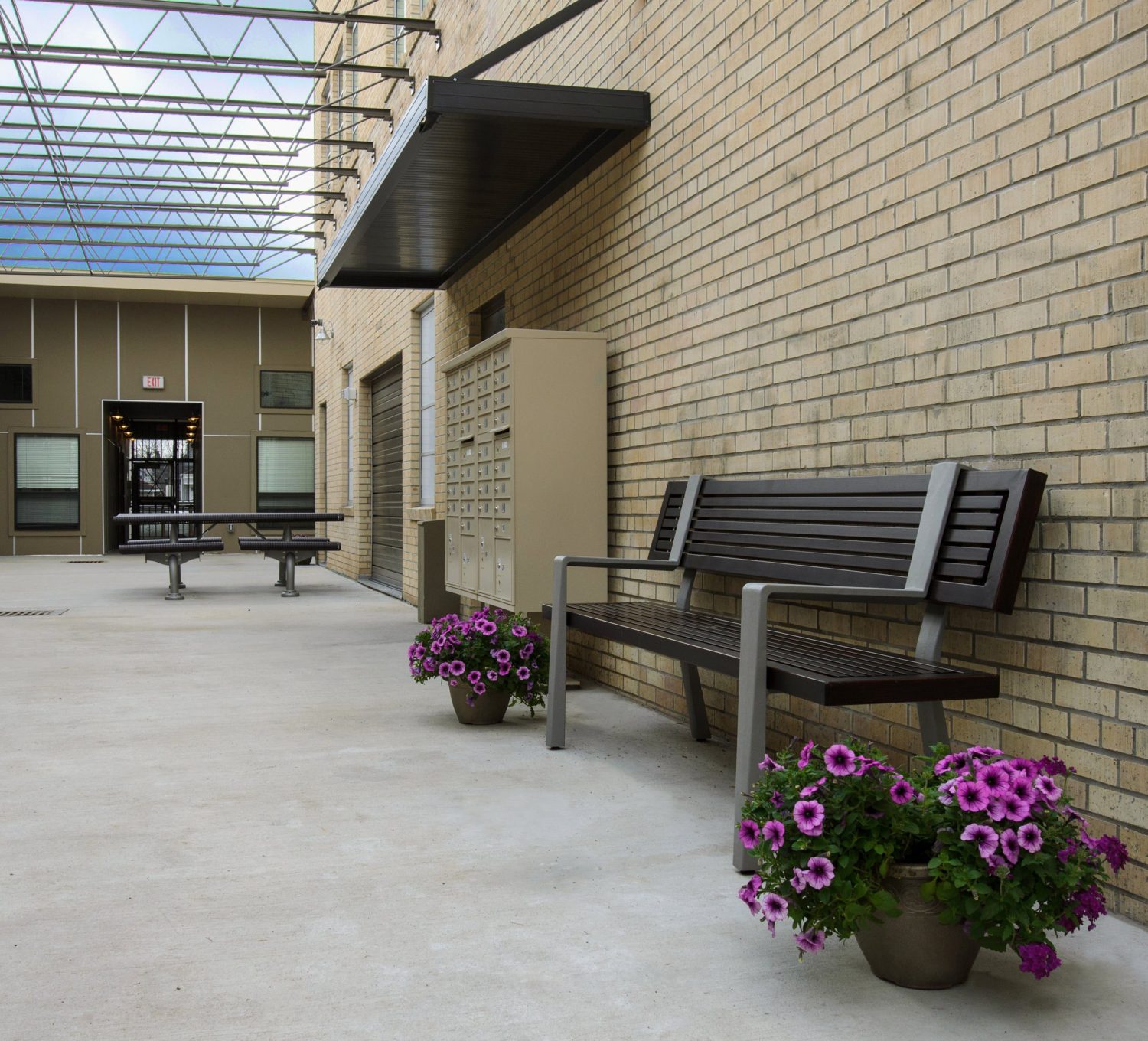 Interior courtyard with bench seating, picnic table, free-standing mail sorter, brick wall, exposed steel beams allow for natural light.