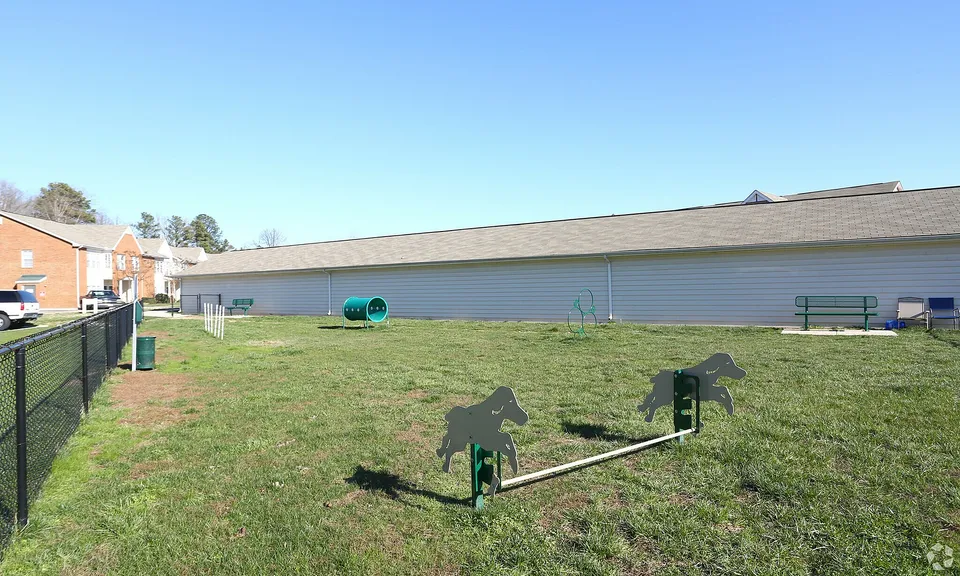 Spacious outdoor dog park with agility equipment and seating in a sunny residential area.