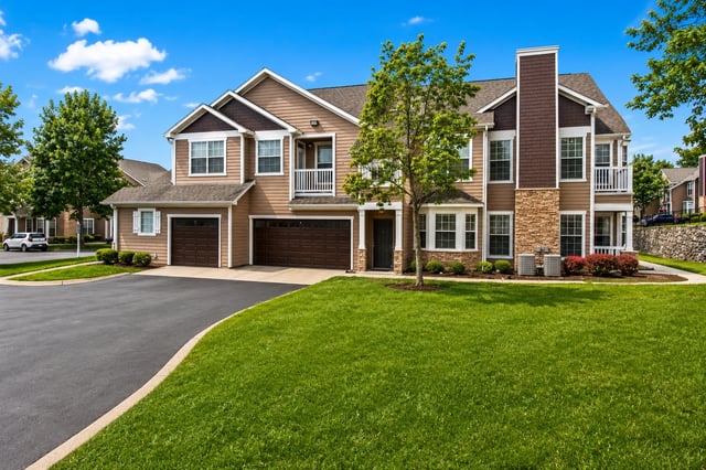 Exterior view of a multi-unit apartment building with attached garages, lush green lawn, and mature…