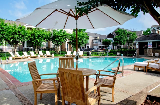 Outdoor swimming pool area with lounge chairs and a dining set under an umbrella.