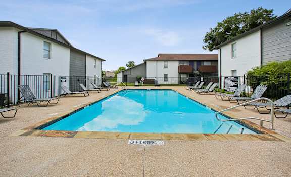 A swimming pool surrounded by chairs and apartment buildings.