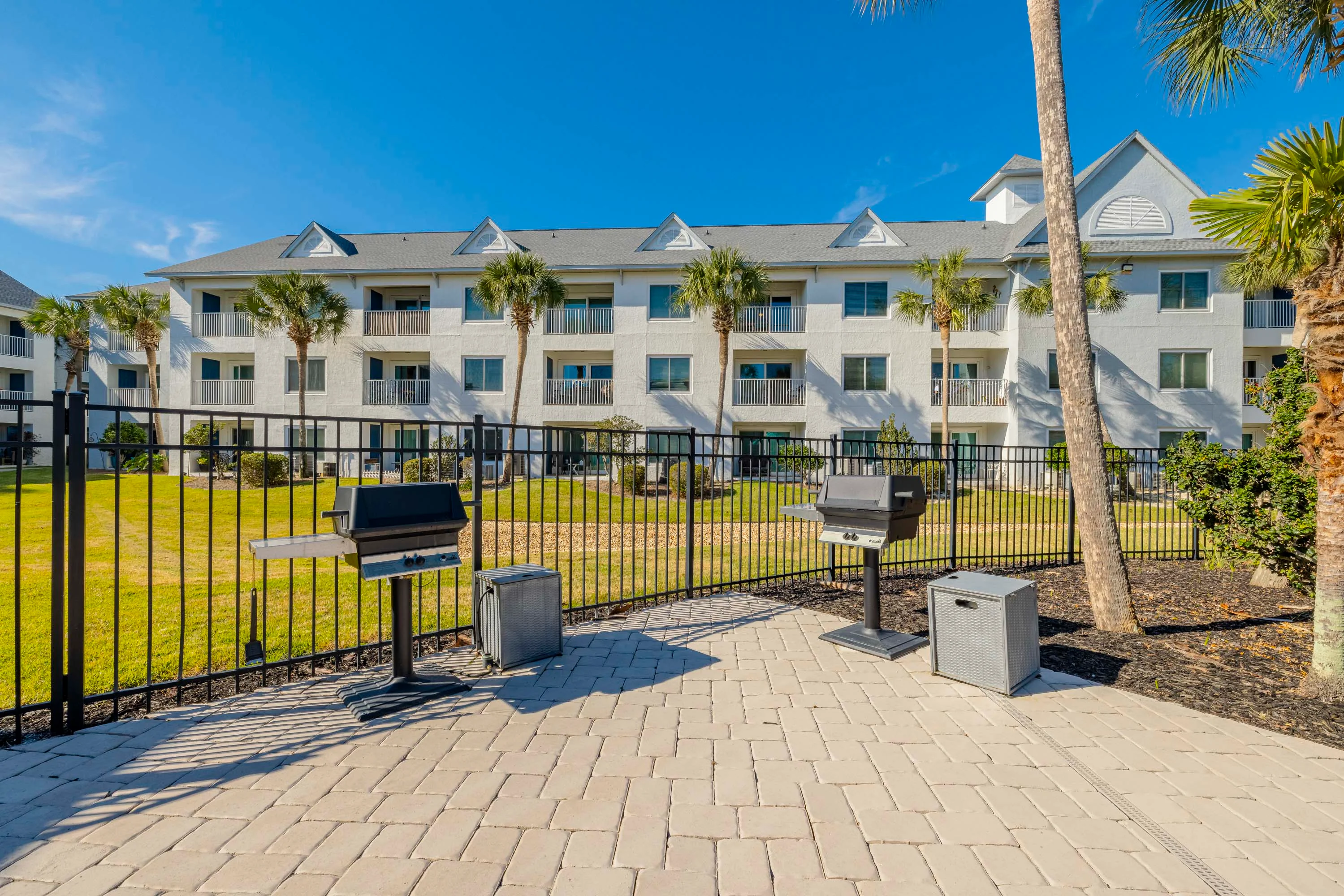 Image of an apartment complex featuring a landscaped yard, outdoor grills, and a clear blue sky. Ideal for gatherings.