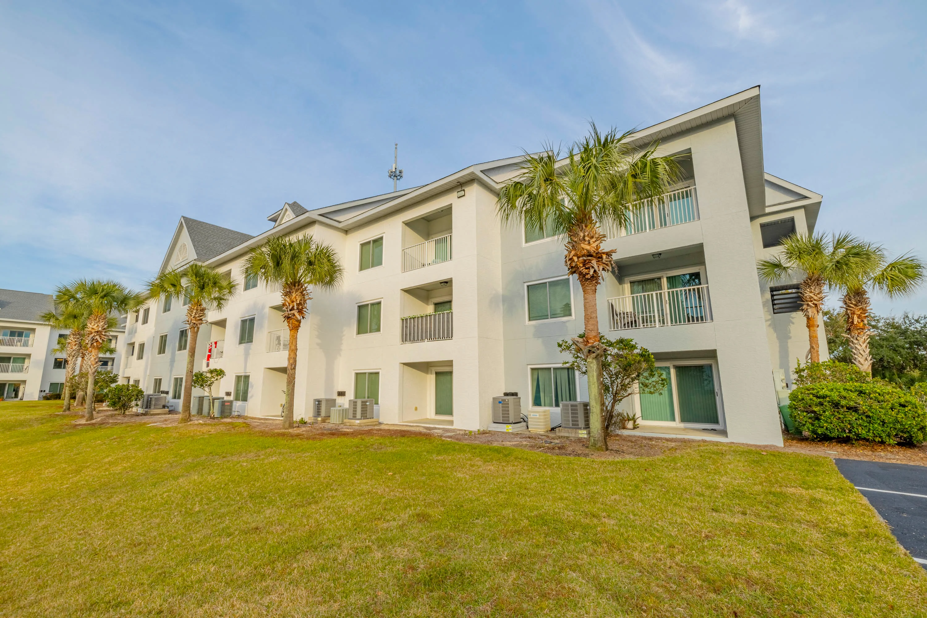 Modern apartment complex with palm trees, green lawns, and balconies under a clear sky. Ideal for comfortable living.