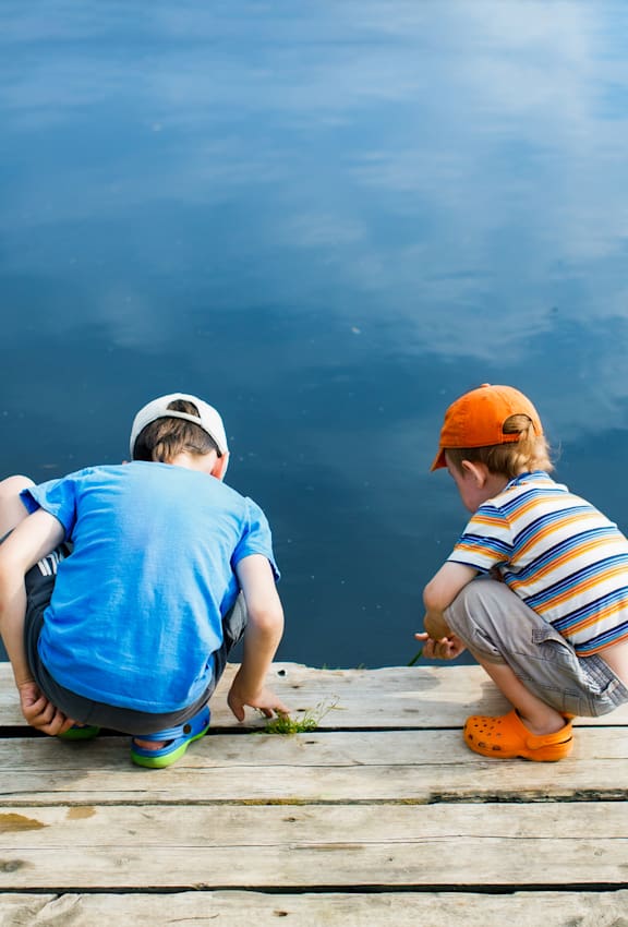 Two children sitting on a dock by the water.