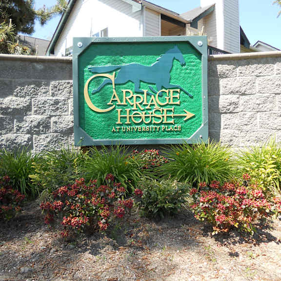 A sign for Carriage House at University Place is displayed in front of a stone wall.