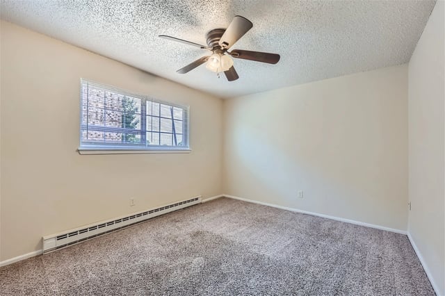 Empty bedroom with beige walls, carpet, a window with blinds, and a ceiling fan.