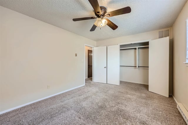 Bedroom interior with ceiling fan, beige walls, and an open double-door closet.