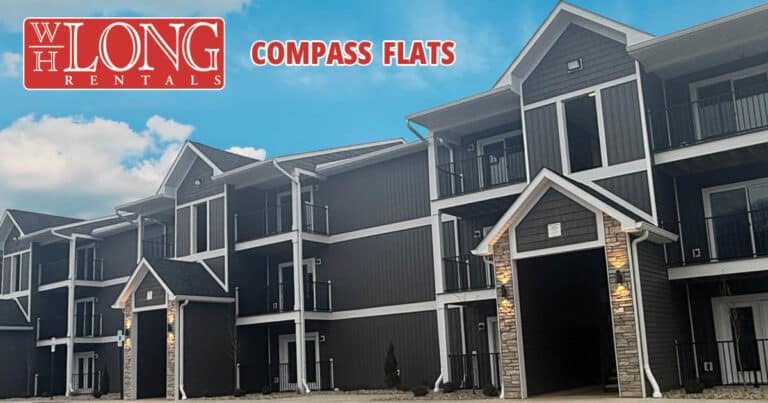 Exterior view of a modern three-story apartment building with balconies, labeled "Compass Flats" and "WH Long Rentals" in the top left corner.