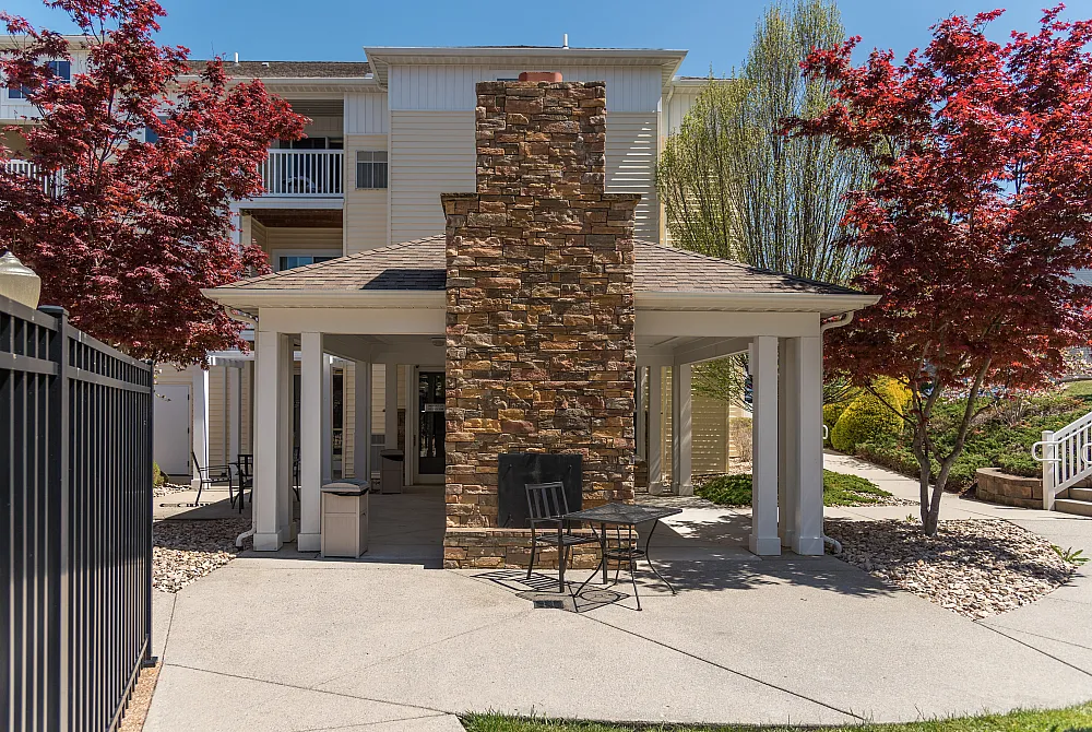 Charming apartment courtyard with a stone fireplace, surrounded by lush trees and modern architecture, perfect for relaxing outdoor gatherings.