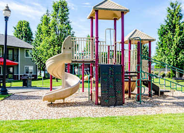 Vancouver, WA Apartments for Rent - Reflections at the Park - Playground with Slide Tower, Surrounding Grassy Lawn, and Trees.